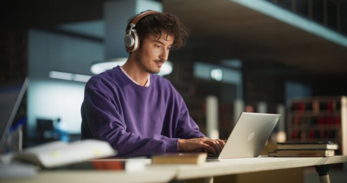 Young male student with headphones on and in front of laptop, typing