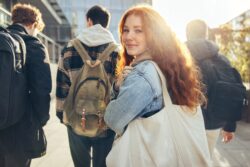 Schoolgirl looking back at camera, holding tote bag. Three male students walking ahead of her.